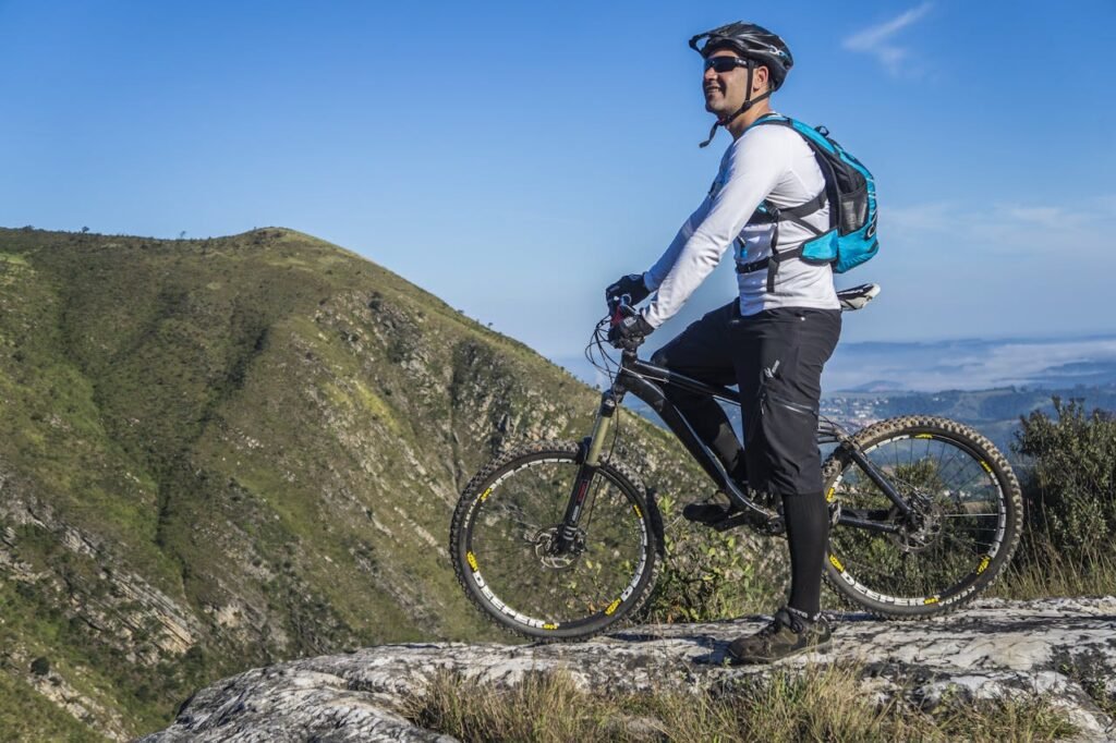 Adult cyclist on mountain bike overlooking scenic rocky landscape under clear blue sky.